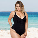 Woman in a black swimsuit standing on a beach with blue water in the background